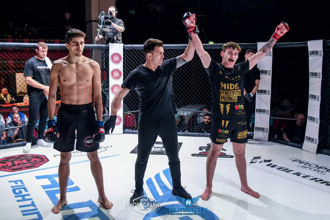 Referee raising the hand of a fighter wearing a gold and black custom 4 Eleven kit