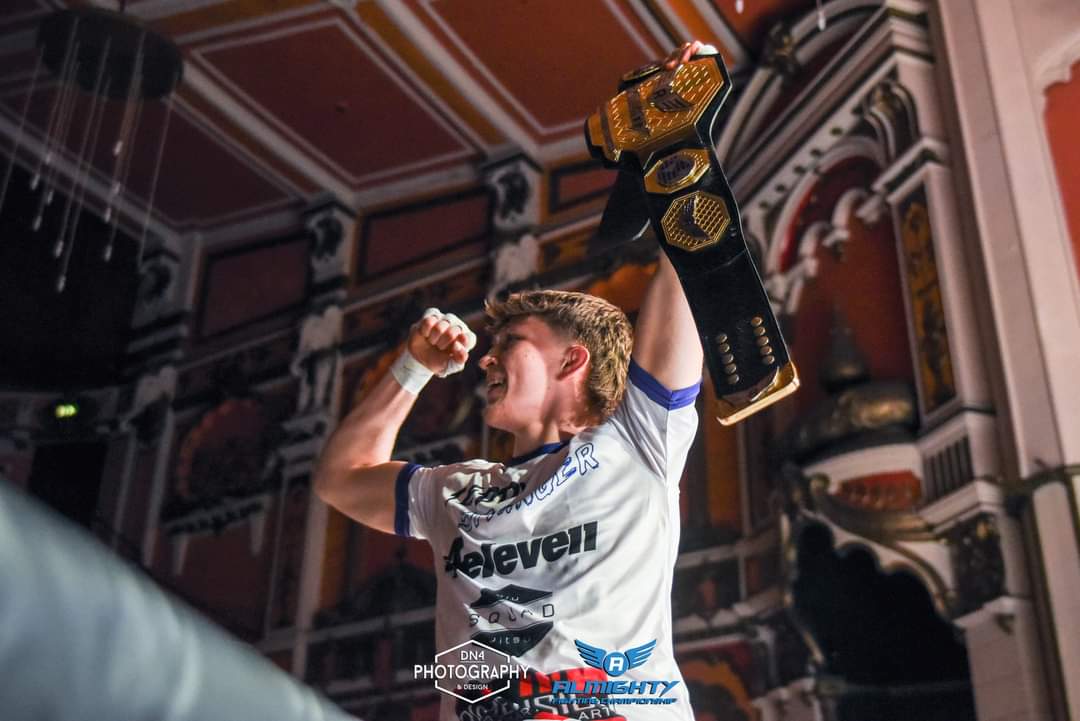 Fighter raising a championship belt above his head in a white 4 Eleven rash guard